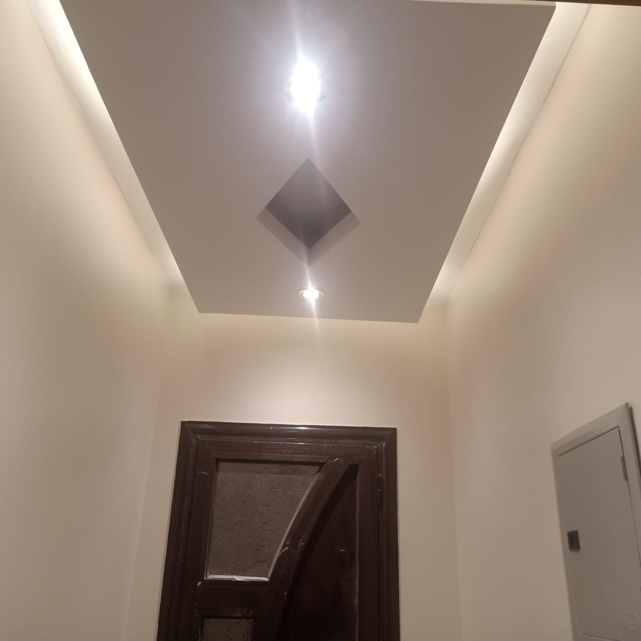 سقف أبيض بتفصيلة هندسية ماسية وإضاءة سبوت داخل فيلا